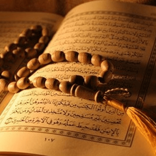 An open page of the Holy Qur’an with wooden prayer beads resting on it.